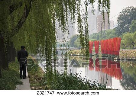 Stock Photo - Man standing on path at edge of pond; Beijing, China. Fotosearch