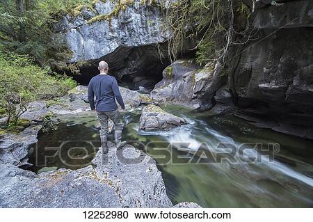 Stock Image - Man standing on rock at the entrance to the Little Huson Caves; Vancouver Island, British Columbia, Canada. Fotosearch