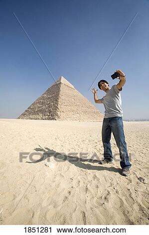 Stock Image - Man Taking A Picture Of Himself With Pyramid In Background. Fotosearch