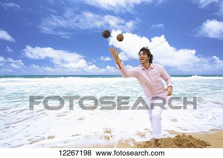 Stock Photo - Man throwing coconuts on the beach; Kealia, Kauai, Hawaii, United States of America. Fotosearch