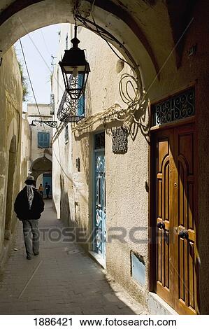 Stock Image - Man Walking Down A Back Alley In Medina. Fotosearch
