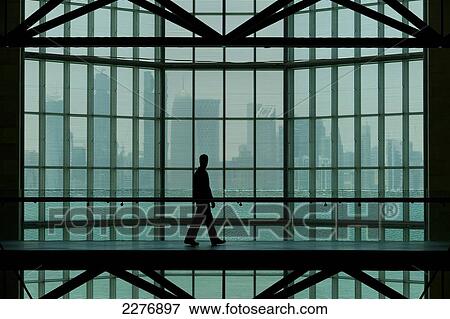 Stock Photo - Man walking past large window in the Museum of Islamic Art, with the skyline of Doha behind, Qatar.. Fotosearch