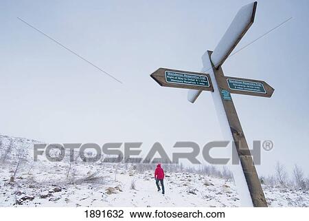 Stock Image - Man Walking Up Hill Near Road Sign, Rear View. Fotosearch