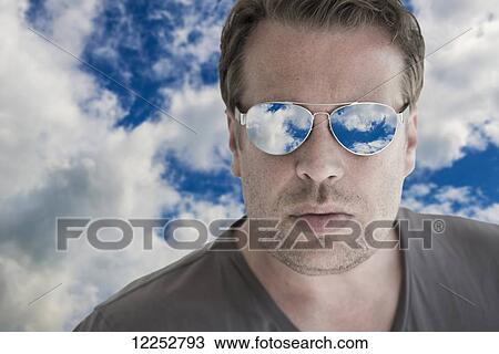 Stock Image - Man wearing sunglasses that are reflecting blue sky and cloud; Locarno, Ticino, Switzerland. Fotosearch