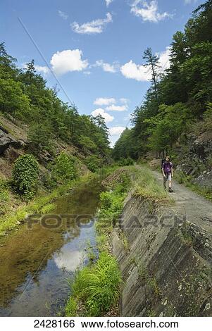 Stock Photograph - Man with backpack hiking along the Chesapeake and Ohio Canal in Western Maryland; Flintstone, Maryland, United States of America. Fotosearch