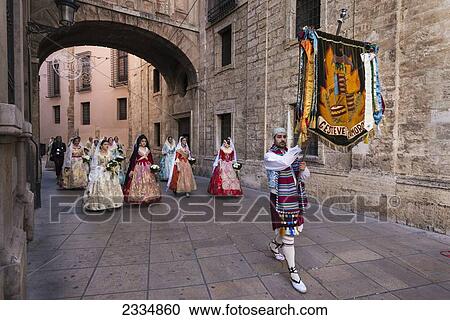 Stock Image - Man With Banner Leading Women Dressed Up In Traditional Casal Faller Outfit With Flower Offering For Virgin De Los Desamparados At Fallas Festival; Valencia, Spain. Fotosearch