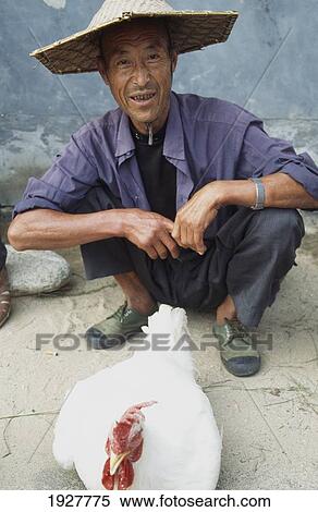 Stock Photography - Man With Cockerel In Market. Fotosearch