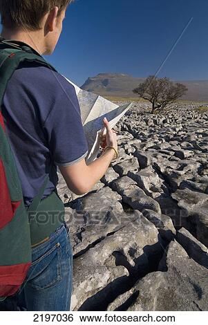 Man With Rucksack Looking At Map On Limestone Pavement With Ingleborough Hill In The Distance Near Ingleton, Yorkshire Dales National Park, North Yorkshire, England. View Large Photo Image Stock Photograph - Man With Rucksack Looking At Map On Limestone Pavement With Ingleborough Hill In The Distance Near Ingleton, Yorkshire Dales National Park, North Yorkshire, England.. Fotosearch