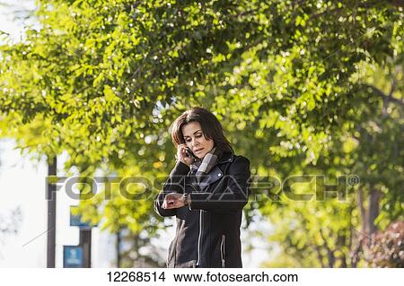 Mature businesswoman talking on her cell phone and checking the time while walking in an urban park outdoors in autumn; Edmonton, Alberta, Canada View Large Photo Image Picture - Mature businesswoman talking on her cell phone and checking the time while walking in an urban park outdoors in autumn; Edmonton, Alberta, Canada. Fotosearch
