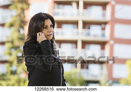 Stock Photograph - Mature businesswoman talking on her cell phone while walking in an urban park outdoors in autumn; Edmonton, Alberta, Canada. Fotosearch