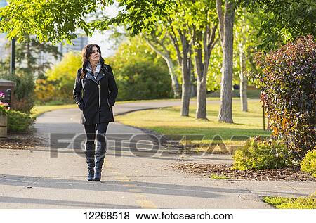 Stock Photo - Mature businesswoman walking outdoors in a city park in autumn; Edmonton, Alberta, Canada. Fotosearch