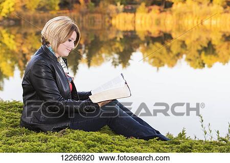 Stock Image - Mature Christian woman studying her Bible in a park beside a lake in autumn; Edmonton, Alberta, Canada. Fotosearch