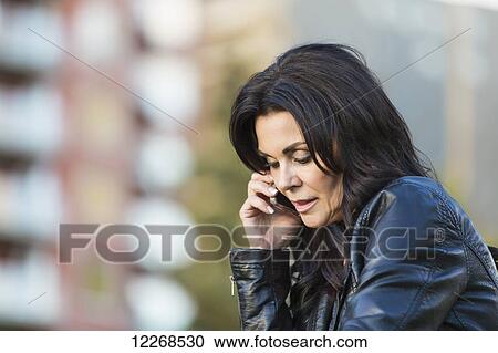 Stock Image - Mature woman talking on her cell phone outdoors in an urban park in autumn; Edmonton, Alberta, Canada. Fotosearch