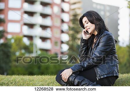 Stock Photo - Mature woman talking on her cell phone outdoors in an urban park in autumn; Edmonton, Alberta, Canada. Fotosearch