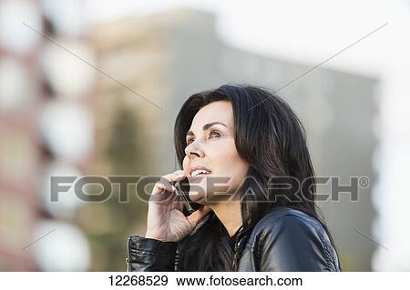 Stock Photo - Mature woman talking on her cell phone outdoors in an urban park in autumn; Edmonton, Alberta, Canada. Fotosearch