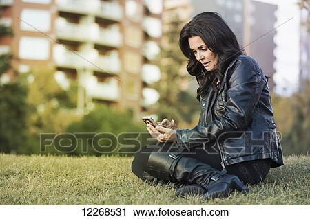 Stock Image - Mature woman texting on her cell phone in an outdoor urban park in autumn; Edmonton, Alberta, Canada. Fotosearch