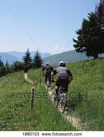 Stock Image - Men Cycling Along Path In The Alps. Fotosearch