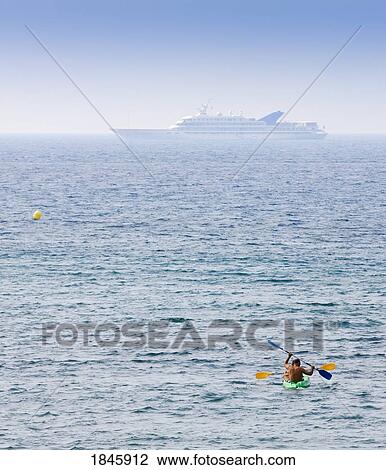 Stock Image - Men In Canoe And Large Yacht In Distance; Marbella, Costa Del Sol, Malaga Province, Spain. Fotosearch