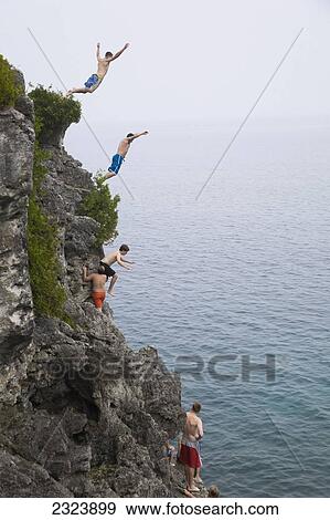 Stock Photo - Men leaping from a cliff into turquoise water of Georgian Bay in Bruce Peninsula National Park; Ontario, Canada. Fotosearch