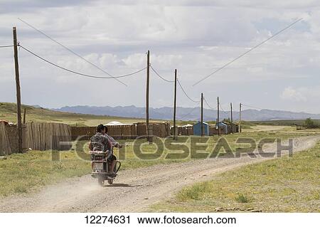 Stock Image - Men on a motorcycle driving by wooden fences and telephone poles, Bulgan, South Gobi Province, Mongolia. Fotosearch