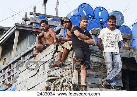 Picture - Men on board of a pinisi, a traditional two masted wooden cargo sailing ship moored in Sunda Kelapa Harbour, Jakarta, Java Island, Indonesia. Fotosearch