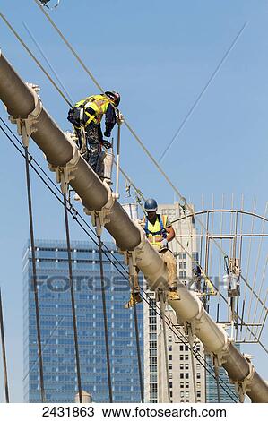 Stock Image - Men painting a suspension cable of the Brooklyn Bridge, New York City, New York, United States. Fotosearch