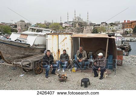 Stock Photo - Men sitting outside a shed on the shore beside a boat on a trailer; Istanbul, Turkey. Fotosearch