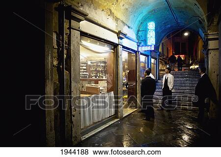 Stock Photo - Men Standing Outside The Entrance Of A Bar At Night; Venice Venezia Italy. Fotosearch
