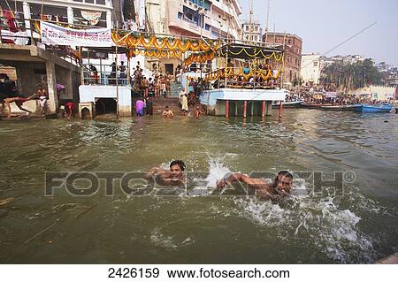 Stock Photo - Men swimming in the Ganges with a view of the Ghats; Varanasi, India. Fotosearch