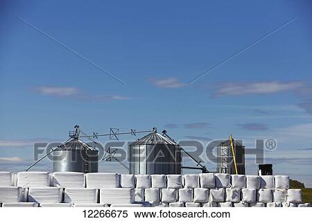 Stock Photography - Metal silos and hay wrapped in white plastic; Quebec, Canada. Fotosearch