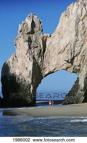Stock Image - Mexico, Cabo San Lucas, Land's End, Couple Walking Under Rock Archway On Beach.. Fotosearch