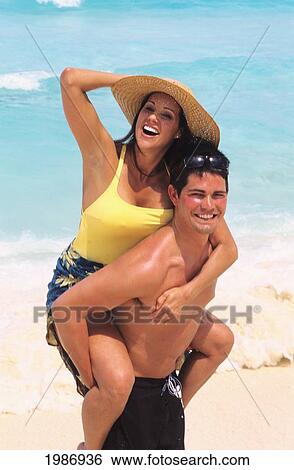 Stock Photograph - Mexico, Cancun, Couple Enjoying Sunny Day On Beach, Man Carrying Woman On Back.. Fotosearch
