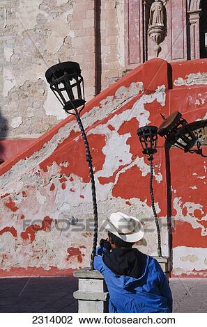 Stock Image - Mexico, Guanajuato, Guanajuato, Man leaning against old lantern. Fotosearch