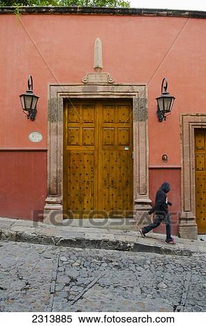 Stock Photography - Mexico, Guanajuato, San Miguel de Allende, Pedestrian walking by old wooden door with large lanterns. Fotosearch