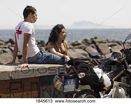 Stock Image - Mid-Adult Couple Sitting On Promenade; Naples, Italy. Fotosearch