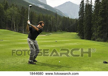 Stock Image - Mid-Adult Man Playing Golf; Canmore, Alberta's Rockies, Alberta, Canada. Fotosearch