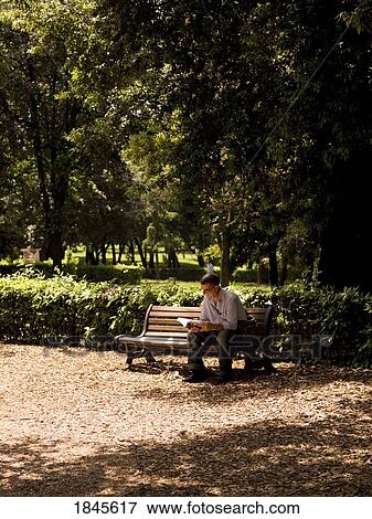Stock Photo - Mid-Adult Man Reading Book In Public Park Near Villa Borghese; Rome, Italy. Fotosearch