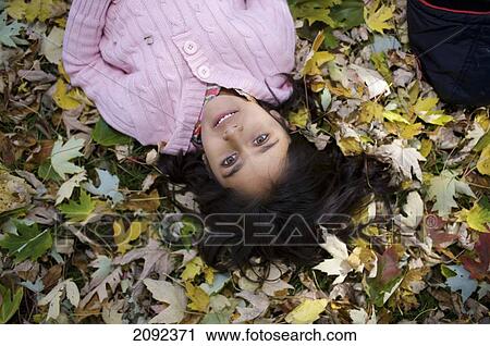 Stock Image - Middle Eastern Girl Lying In Autumn Leaves Outside Esl School; Guelph Ontario Canada. Fotosearch