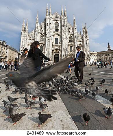 Stock Photo - Milan Cathedral with people feeding birds in the foreground; Milano, Italy. Fotosearch