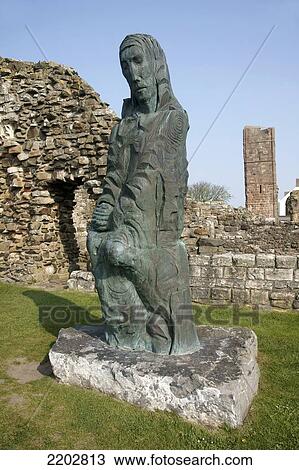 Stock Image - Modern statue of Saint Cuthbert of Farne in the ruins of Lindisfarne Priory; Lindisfarne, Northumberland, England. Fotosearch
