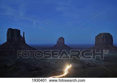 Stock Image - Monument Valley, Utah, Usa Car Headlights Glow At The Base Of The Left And Right Mitten And Merrick Butte In Monument Valley Straddling The Utah/Arizona State Border.. Fotosearch