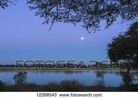 Stock Image - Moon setting over the Shire River at dawn, Liwonde National Park; Malawi. Fotosearch