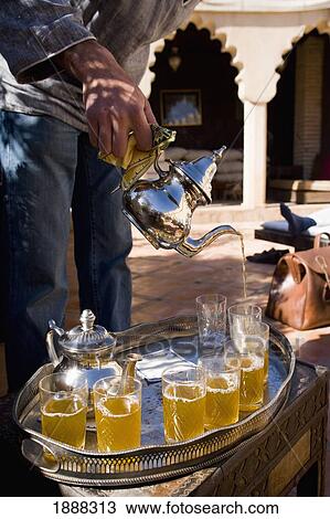 Stock Image - Moroccan Waiter Pouring Traditional Mint Tea In Courtyard. Fotosearch
