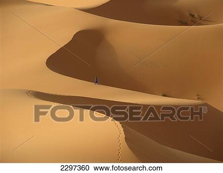 Stock Image - Morocco, Berber 'blue man' walking through sand dunes in Erg Chebbi area; Sahara Desert near Merzouga. Fotosearch