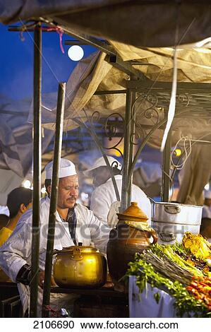 Stock Image - Morocco, Cook serving food at stall in Djemaa el-Fna Square; Marrakech. Fotosearch