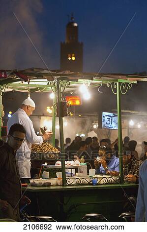 Stock Image - Morocco, Cook serving food at stall in Djemaa el-Fna Square; Marrakech. Fotosearch