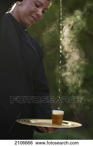 Stock Photograph - Morocco, Dar Ahlam Hotel; Skoura, Waitress pouring Moroccan mint tea into glass from height. Fotosearch