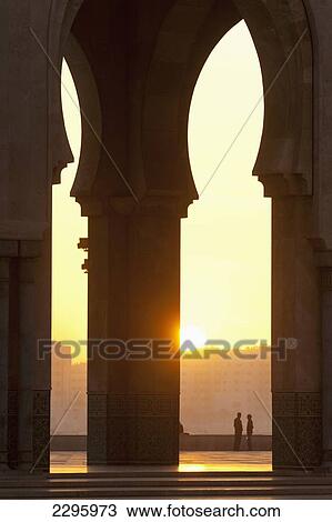 Stock Image - Morocco, Looking through arches of Hassan II mosque to couple chatting; Casablanca. Fotosearch