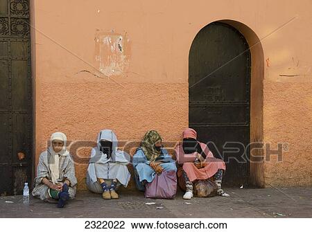 Stock Image - Morocco, Marrakech, Medina, Women sitting along wall together. Fotosearch