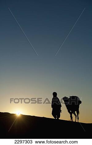 Morocco, Silhouette of Berber 'Blue man' leading camel across sand dunes at dusk in Erg Chebbi area; Sahara Desert near Merzouga View Large Photo Image Stock Image - Morocco, Silhouette of Berber 'Blue man' leading camel across sand dunes at dusk in Erg Chebbi area; Sahara Desert near Merzouga. Fotosearch